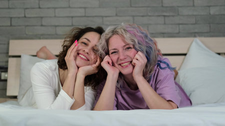 Portrait of two women with curly hair and bright makeup relaxing at home together. Female friendship conceptの写真素材