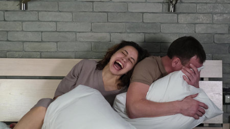 Married couple having fun sitting on their bed at home. A man and a woman laugh in the bedroom in...