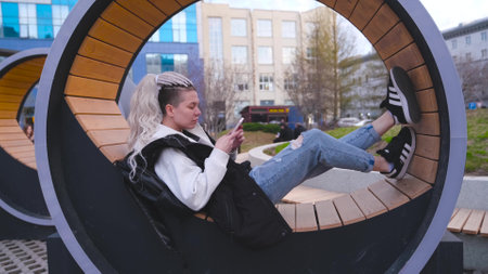 A woman with dreadlocks sits in a city park and looks at her smartphone.