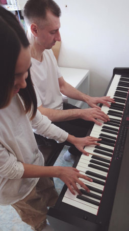 A teenage pianist and her dad play the piano, touching their fingers to the black and white keys to create the rhythm of the melody. People. Child development and entertainment. Art. Educationの写真素材