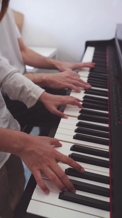 A teenage pianist and her dad play the piano, touching their fingers to the black and white keys to create the rhythm of the melody. People. Child development and entertainment. Art. Educationの写真素材