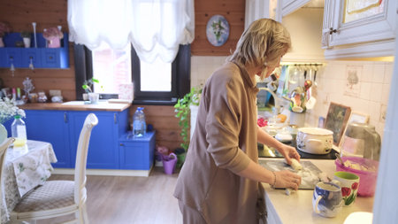Happy attractive young woman housewife preparing breakfast for family. Mom stands near the kitchen stove and prepares dinnerの写真素材