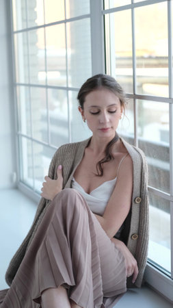 Beautiful young girl posing for the camera while sitting near a large windowの写真素材