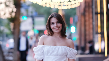 Portrait of a young woman in a cute white dress on a city street in the eveningの写真素材