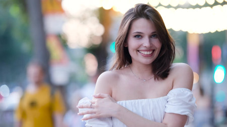 Portrait of a beautiful young woman in a cute white dress on a city street in the eveningの写真素材