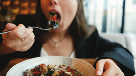 Dinner at a restaurant. A woman eats an eggplant and cheese salad with appetite. Close-up.
