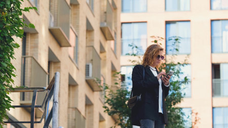 Caucasian woman with curly hair using her mobile phone outdoors. Close-up. Communication technology and modern lifestyle conceptの写真素材