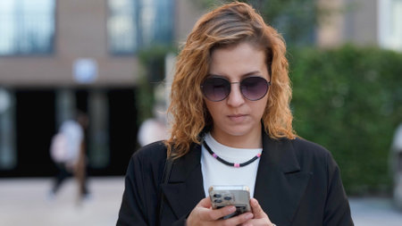 Caucasian woman with curly hair using her mobile phone outdoors. Close-up. Communication technology...