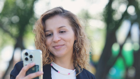 Caucasian woman with curly hair using her mobile phone outdoors. Close-up. Communication technology and modern lifestyle conceptの写真素材