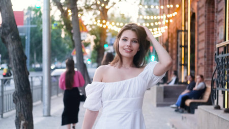 Portrait of a beautiful young woman in a white dress on a city street in the eveningの写真素材