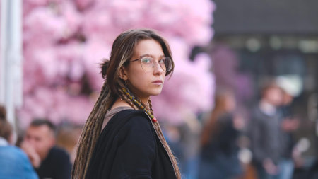 Portrait of a young woman with dreadlocks on a city street. A girl is sitting on the street in the food court area with a glass of coffee in her hand. She is getting ready to meet her friends.の写真素材