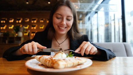 A woman eats fresh strudel with vanilla ice cream, just baked, sitting at a table in a cafe, enjoying a break or breakfast.の写真素材