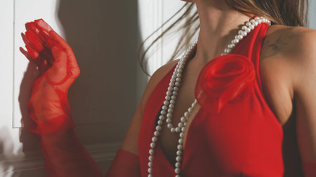 Portrait of a young model posing in lingerie, in red gloves and a vest, with white pearl beads on her neck. Calm brunette in fashionable lingerie.の写真素材