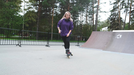 Cute blonde feels free and light while roller skating alone in city park. Stunning Caucasian woman...