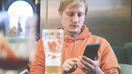Close-up of man using smartphone while drinking beer in pub.の写真素材
