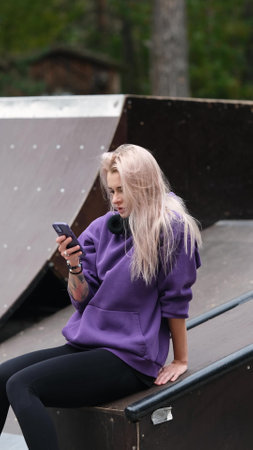 Blonde feels free and light while rollerblading alone in the city park. She is relaxing on the playground wearing roller skates. Stunning woman with a beautiful figure uses roller skates for outdoor sports.の写真素材