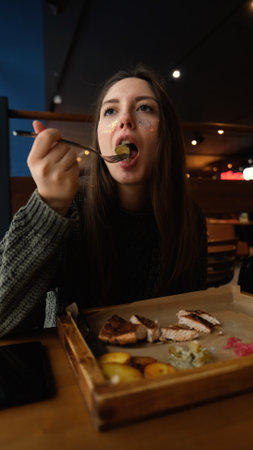 Pretty brunette enjoying tasty beef steak in restaurant in winter. Woman in warm cozy sweater eating...