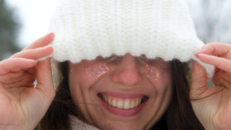 Portrait of a beautiful young woman in winter clothes. The woman smiles happily against the background of a snowy parkの写真素材