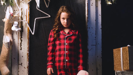 Portrait of sad dissatisfied little girl in night pajamas holding teddy bear in hands. Child disappointed with gifts from Santa Claus. Christmas night, festive atmosphereの写真素材