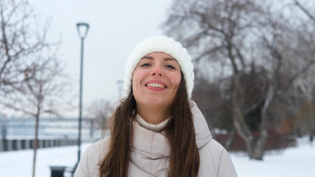Portrait of woman in warm white knitted hat outdoors in winter. Young woman smiling and enjoying...