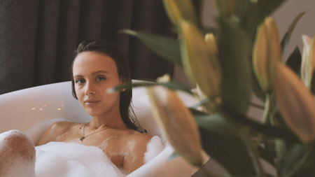 A young woman takes a luxurious bubble bath near a large window â€“ a moment of relaxation and...