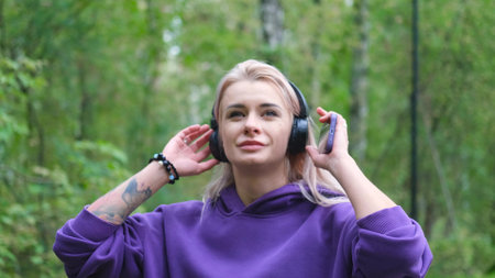 Blonde in purple sweatshirt listening to music on headphones while breathing fresh air in forestの写真素材