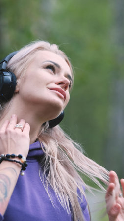 Blonde in purple sweatshirt listening to music on headphones while breathing fresh air in forestの写真素材