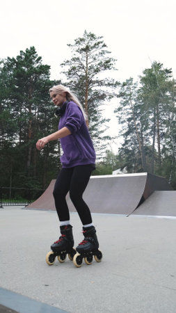 Blonde feels free and light while roller skating alone in city park. Woman with beautiful figure...