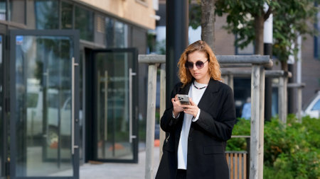 Caucasian woman with curly hair using her mobile phone outdoors. Close-up. Communication technology...