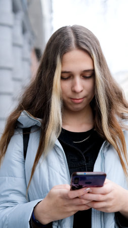 Sad teenage girl feeling frustrated texting on her smartphone standing on city streetの写真素材