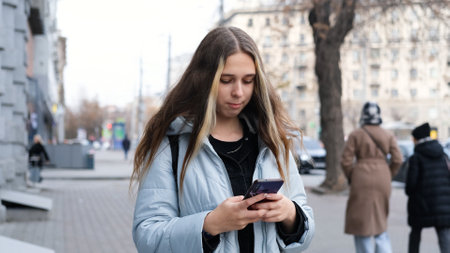 Teenage girl feeling frustrated texting on her smartphone standing on city streetの写真素材