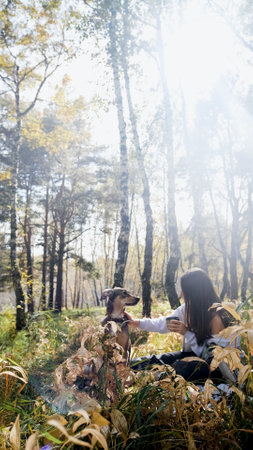 A sweet young woman with her dog enjoys the beauty of nature and the bond with her pets. The woman drinks tea from a thermosの写真素材