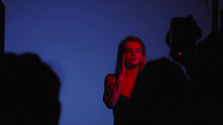 Blonde with a beautiful figure in a black patent leather bodysuit poses in a studio. Studio lighting, low exposure, monochrome red lightの写真素材