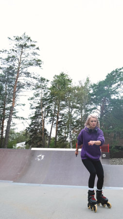 Cute blonde feels free and light while roller skating alone in city park. Caucasian woman with...