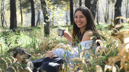 A sweet young woman with her dog enjoys the beauty of nature and the bond with her pets. The woman...