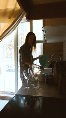 Woman washes glasses under running water, washes dishes in kitchen sinkの写真素材