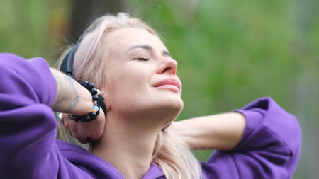 Blonde in purple sweatshirt listening to music on headphones while breathing fresh air in forestの写真素材