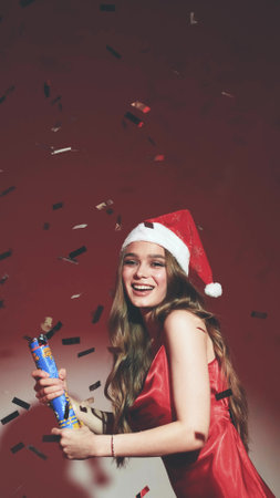 Happy woman with long hair in New Years hat and red dress posing on red background at New Years party style photo shootの写真素材