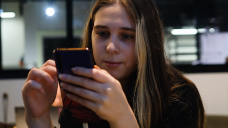 Young teenage girl sitting in modern cafe, using her smartphone to browse internet, check social media or send messages, enjoying the moment of digital connection in a cozy environment.の写真素材