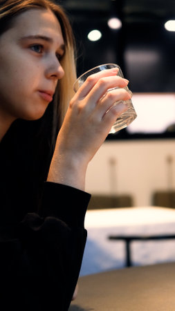 Young teenage girl drinks water from a transparent glass