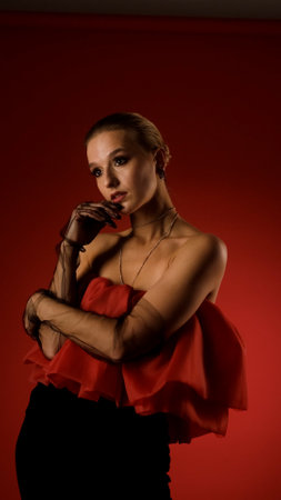 Portrait of photo model posing in red dress and black transparent gloves. Girl on red background.の写真素材