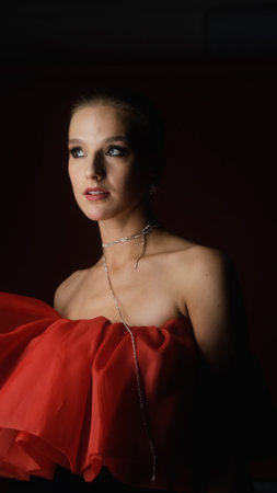 Portrait of photo model posing in red dress and black transparent gloves. Girl on red background.の写真素材