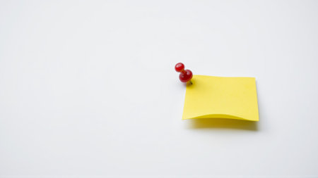 A yellow sheet of paper for notes is attached with a red pushpin to a white wallの素材