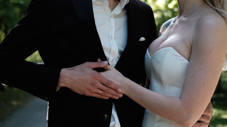 Loving bride and groom pose for the camera during a wedding photo shoot in the park. The brides hand passionately caresses her grooms chest, close-upの写真素材