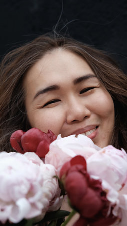 Portrait of a beautiful smiling woman with a bouquet of peonies in her hands. close-up.の写真素材