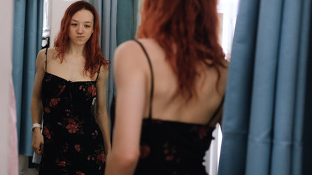 Young teenage girl trying on a dress in a fitting room of a clothing storeの写真素材