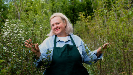 Portrait of happy female gardener standing among bright greenery of her gardenの写真素材