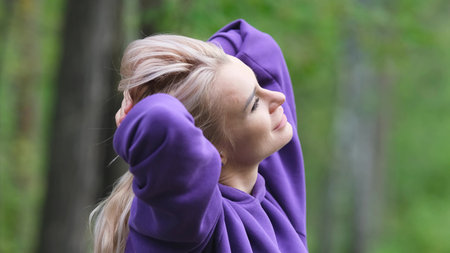 Blonde in purple sweatshirt doing morning exercises, breathing fresh air in forestの写真素材