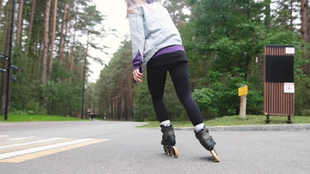 Cute blonde feels free and light while roller skating alone in city park. Stunning Caucasian woman with beautiful figure uses roller skates for outdoor sports.の写真素材
