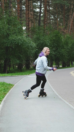 Cute blonde feels free and light while roller skating alone in city park. Stunning Caucasian woman...